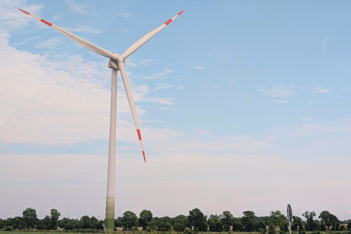 Windrad auf der linken Bildhälfte, im Hintergrund blauer, leicht bewölkter Himmel.