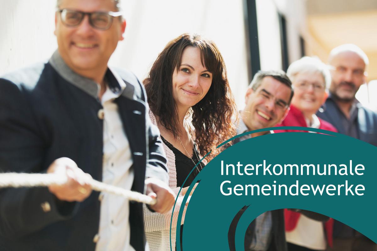 Fünf Personen ziehen gemeinsam lachend an einem Seil. Rechte untere Ecke: Blauer Farbbanner mit dem Schriftzug "interkommunale Gemeindewerke"