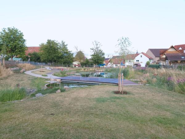 Über einen Wasserlauf führt eine Metallbrücke. Im Hintergrund: die Häuser und Kirche von Waldfenster.