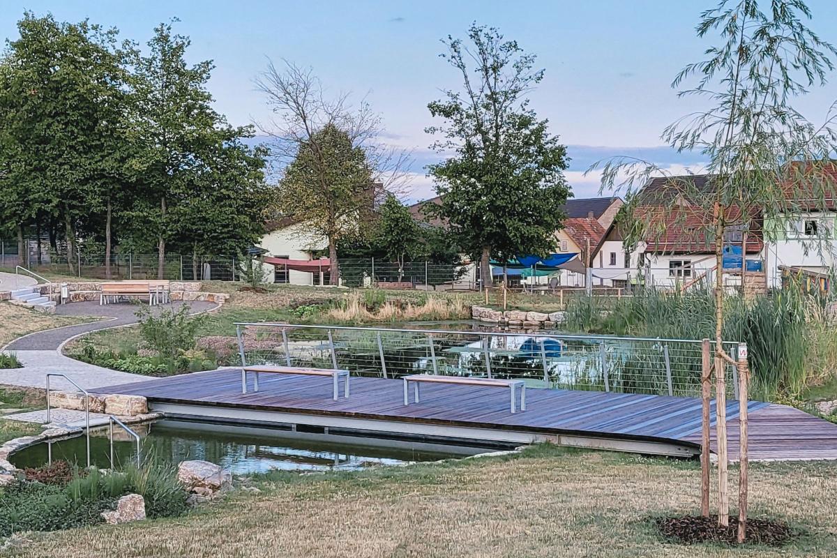 Holzbrücke mit Sitzgelegenheiten beim Dorfsee.