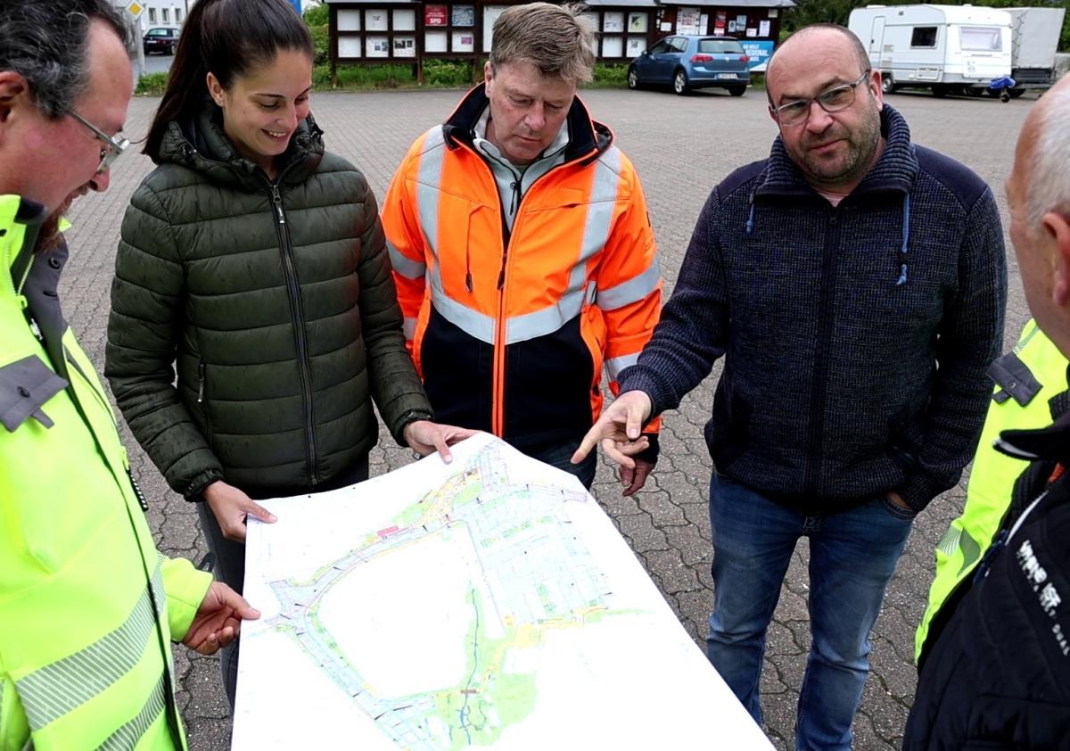5 Personen halten Bauplan in der Hand und diskutieren darüber