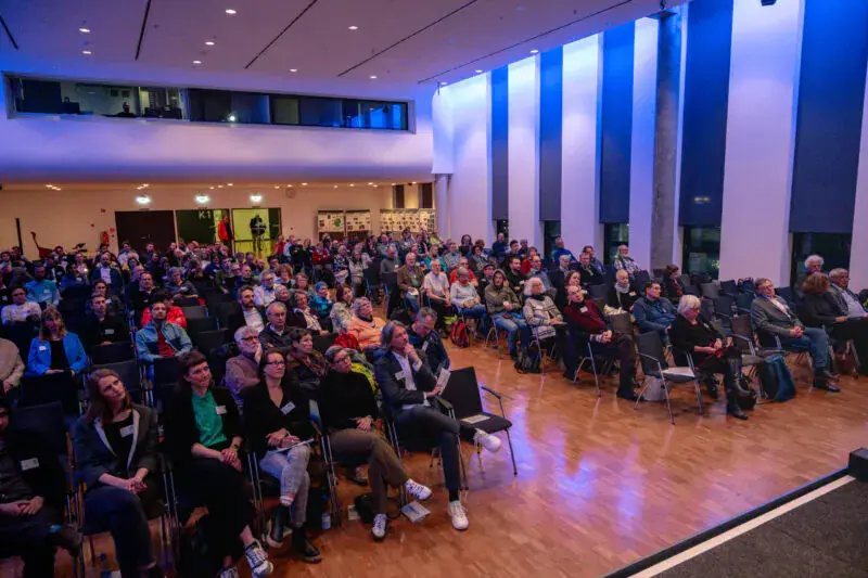 Personen sitzen auf Stühlen in einem Saal.