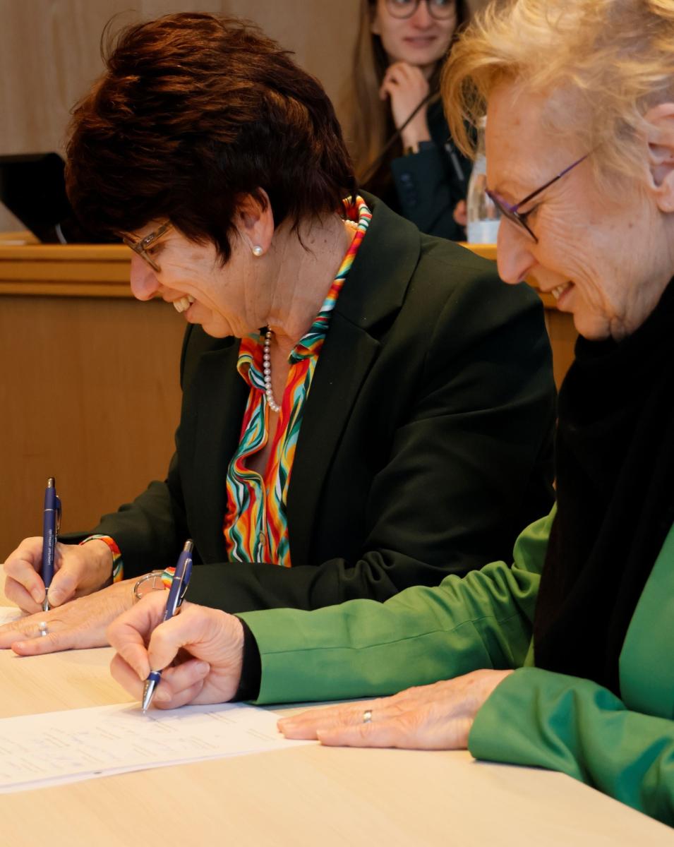 Zwei Frauen unterschreiben lachend einen Vertrag.