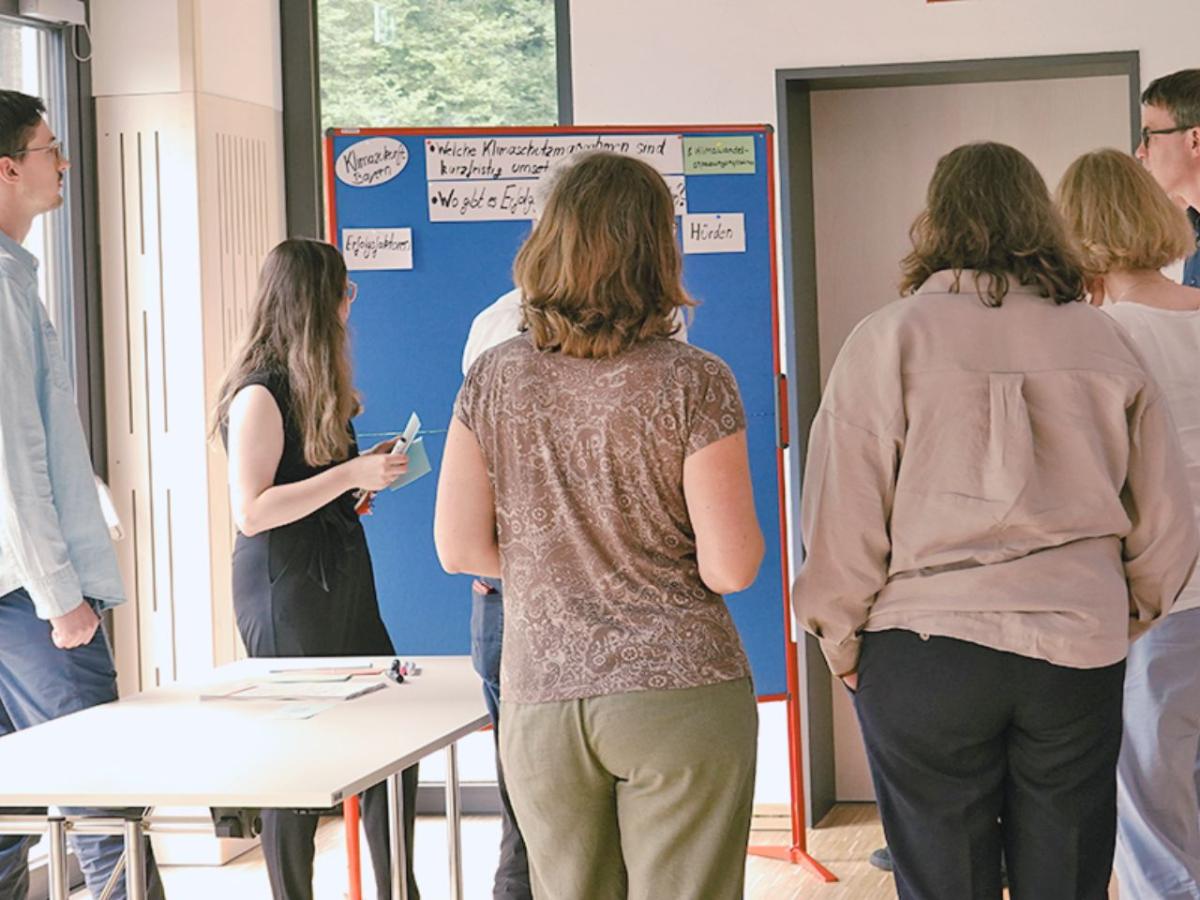 Personen stehen um Pinnwand und bearbeiten Fragen