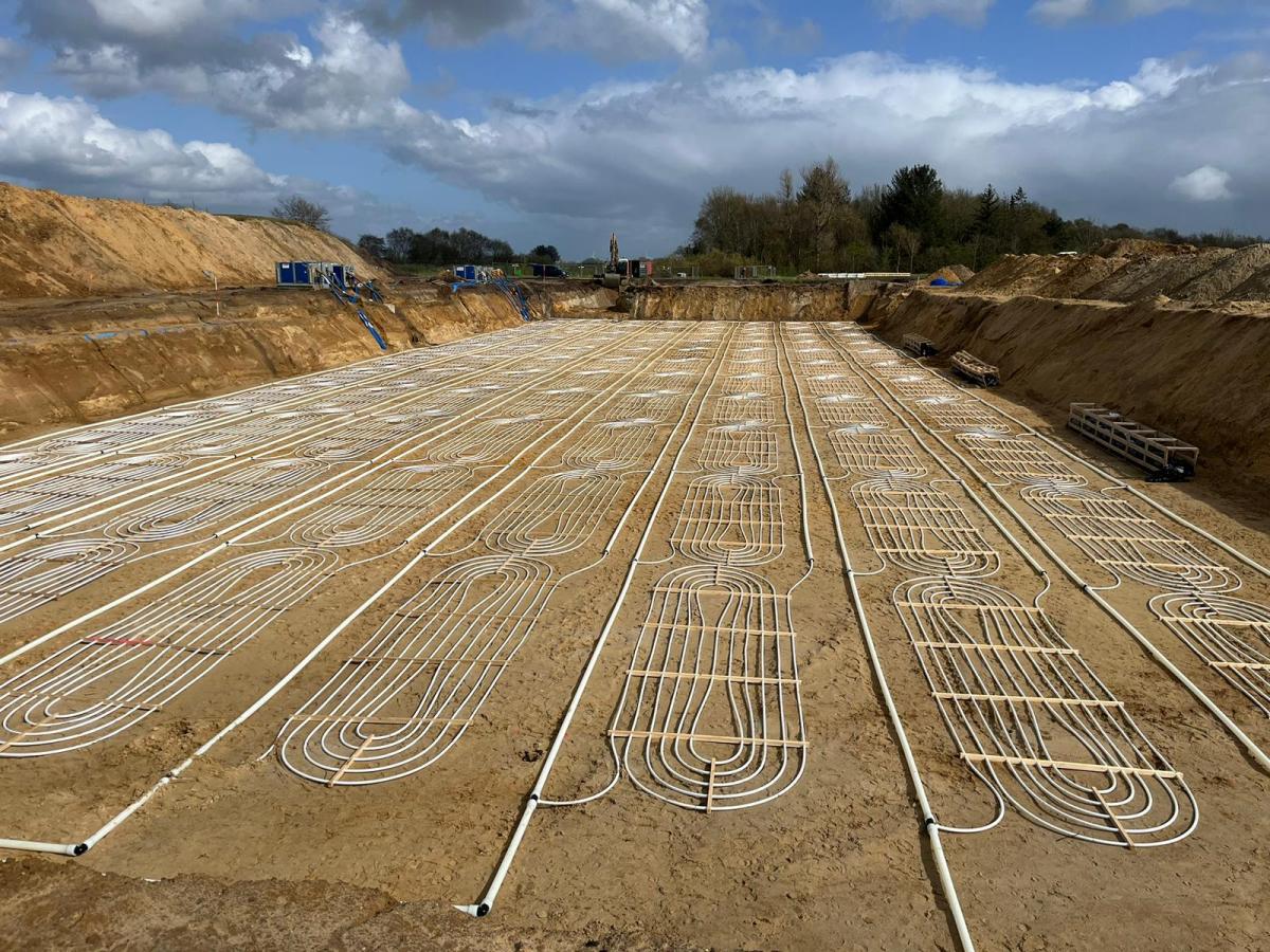 Horizontale Flachkollektoren in Erdaushub vor einem Dorf.