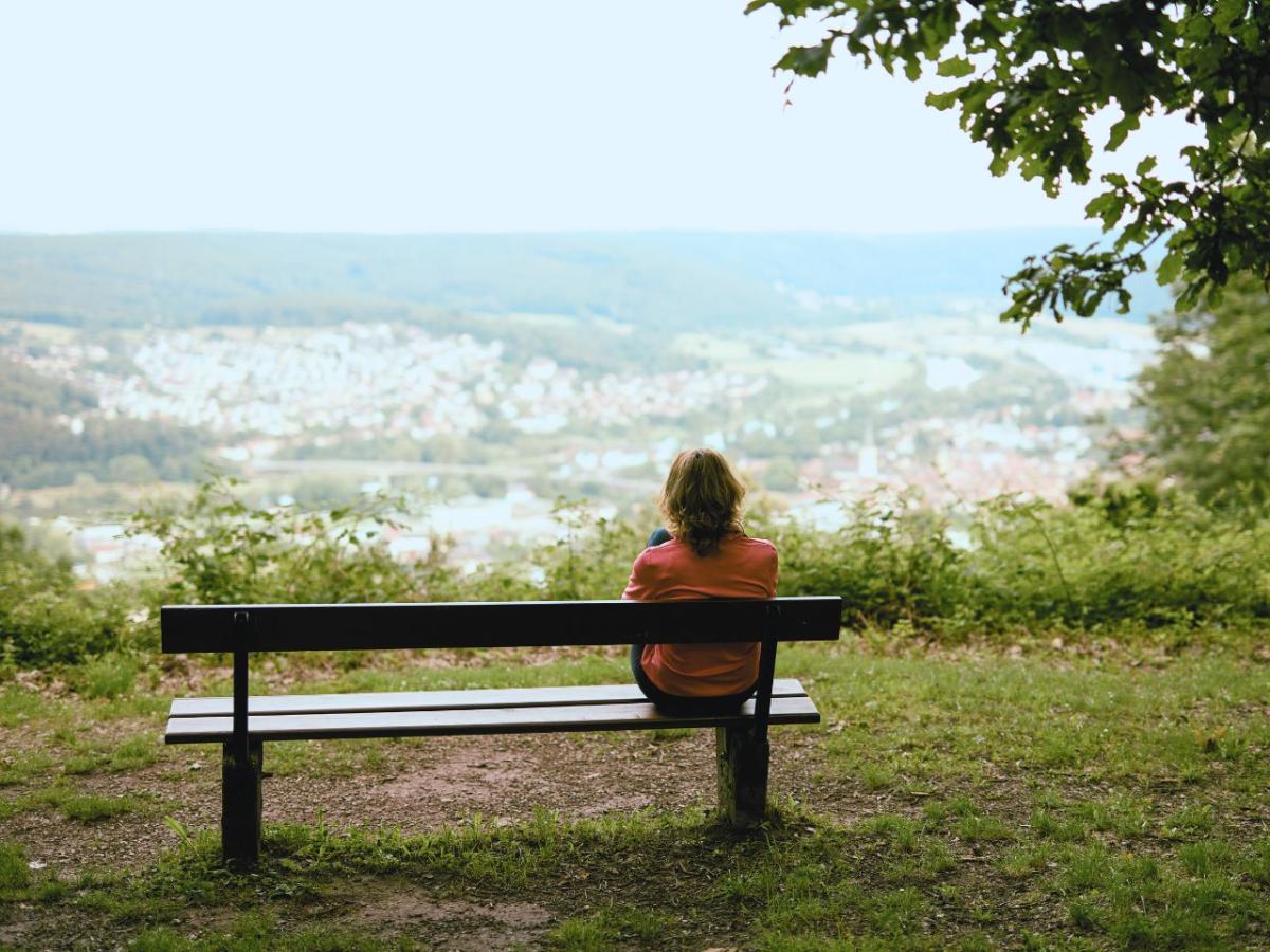 Joggerin sitzt auf einer Ruhebank im Wald und genießt den Ausblick ins Tal