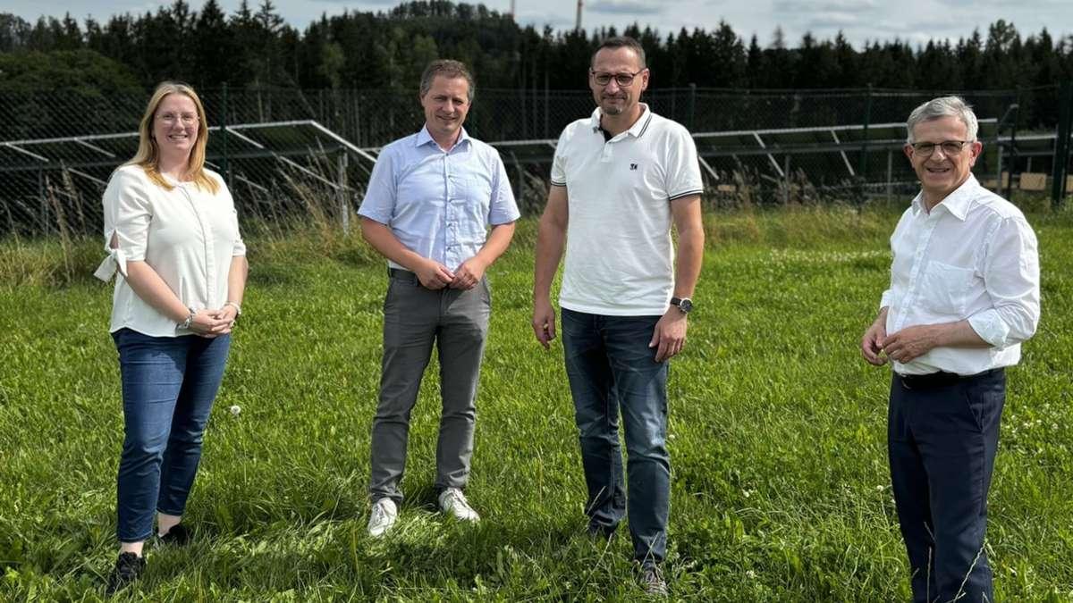 Vier Menschen stehen auf einer Wiese. Im Hintergrund PV und Windkraftanlagen.
