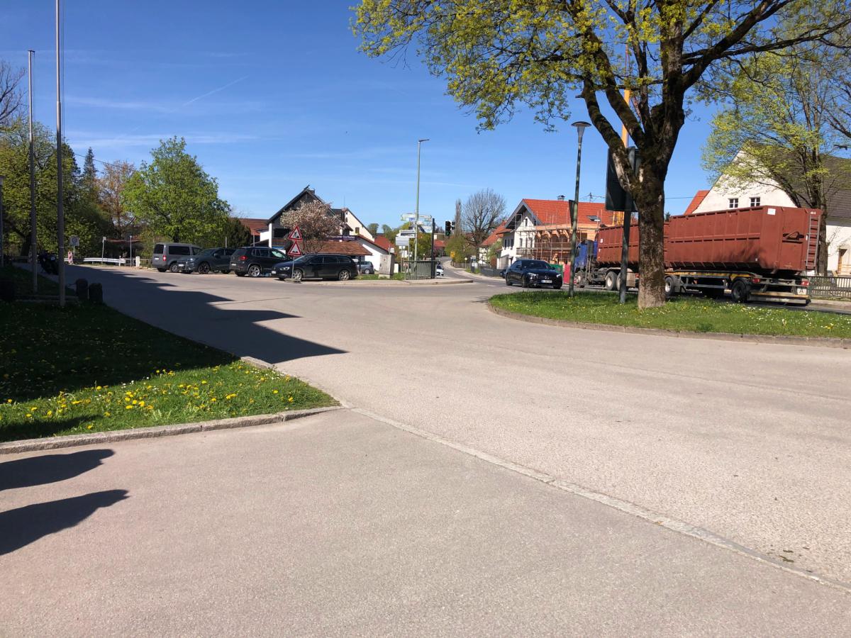 Versiegelter Dorfplatz mit Baum. Im Hintergrund ein LKW.