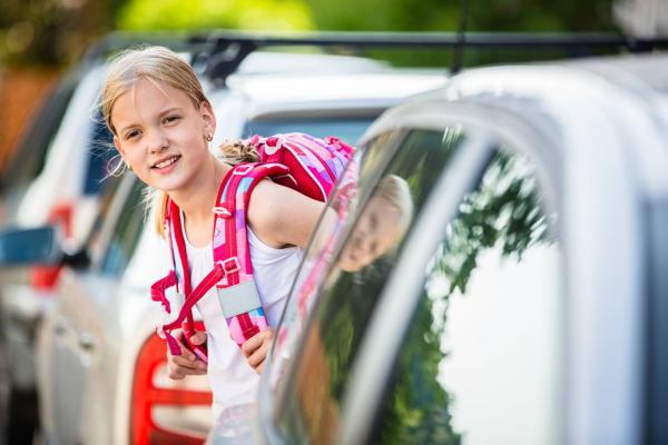 Schulmädchen steht zwischen Autos und sieht in die Kamera.