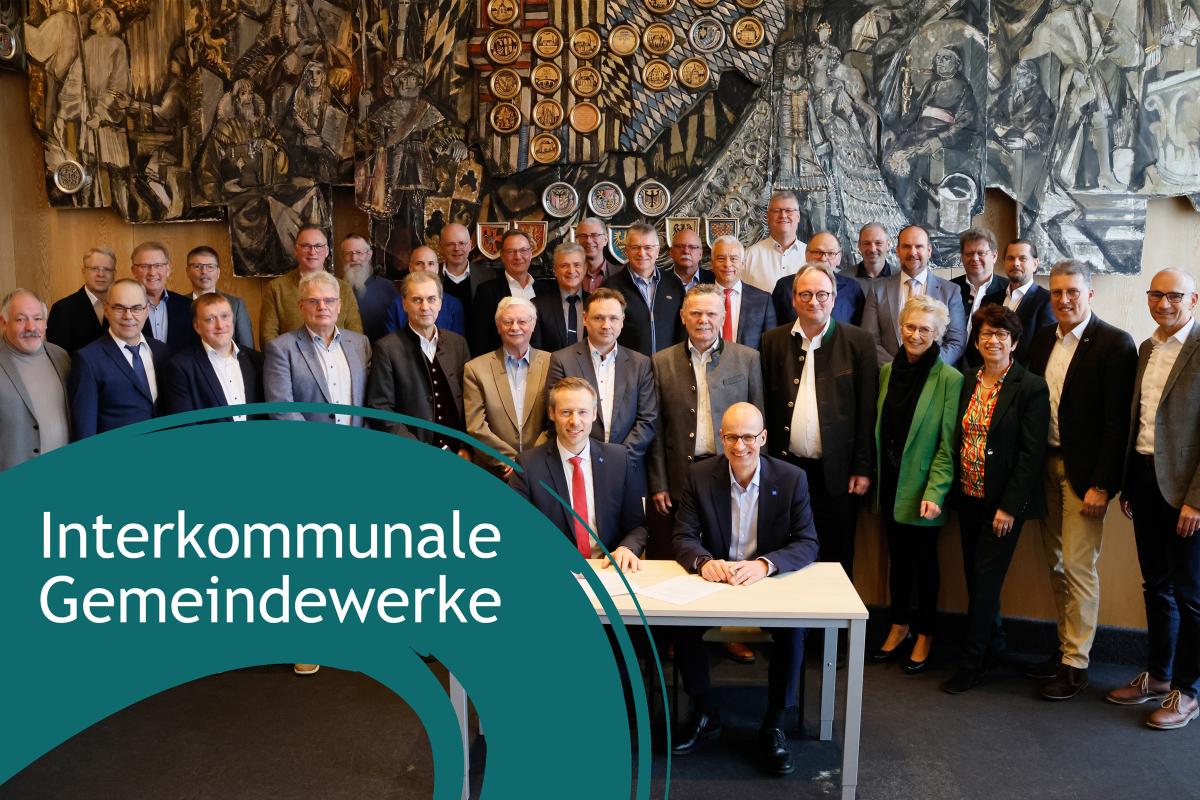 Mehrere Menschen stehen um einen Tisch und lächeln in die Kamera. Links unten: Blauer Farbkleks mit Schriftzug.