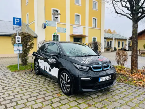 Schwarzes Elektroauto lädt an Ladesäule auf einem Parkplatz vor einem gelben Gebäude