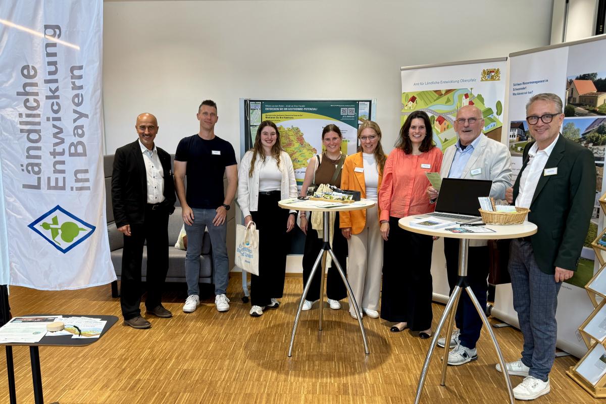 Acht Personen vor einem Messestand lachen gemeinsam in die Kamera.