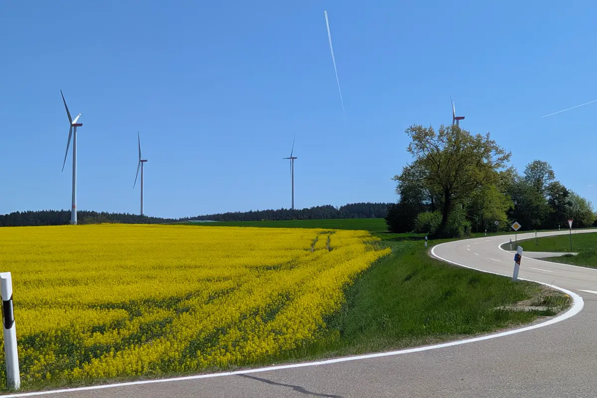 Im Hintergrund ein gelbes Rapsfeld und vier Windkraftanlagen bei blauem Himmel. Linke obere Ecke: Blauer Farbbanner mit dem Schriftzug "interkommunale Gemeindewerke"
