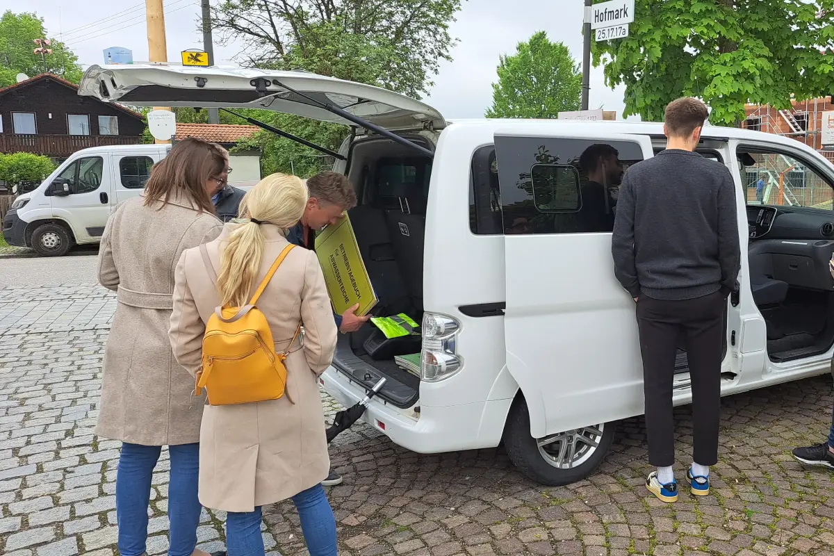 Personen besichtigen einen weißen Bürgerbus. Im Hintergrund Bäume und ein weiterer weißer Bus.