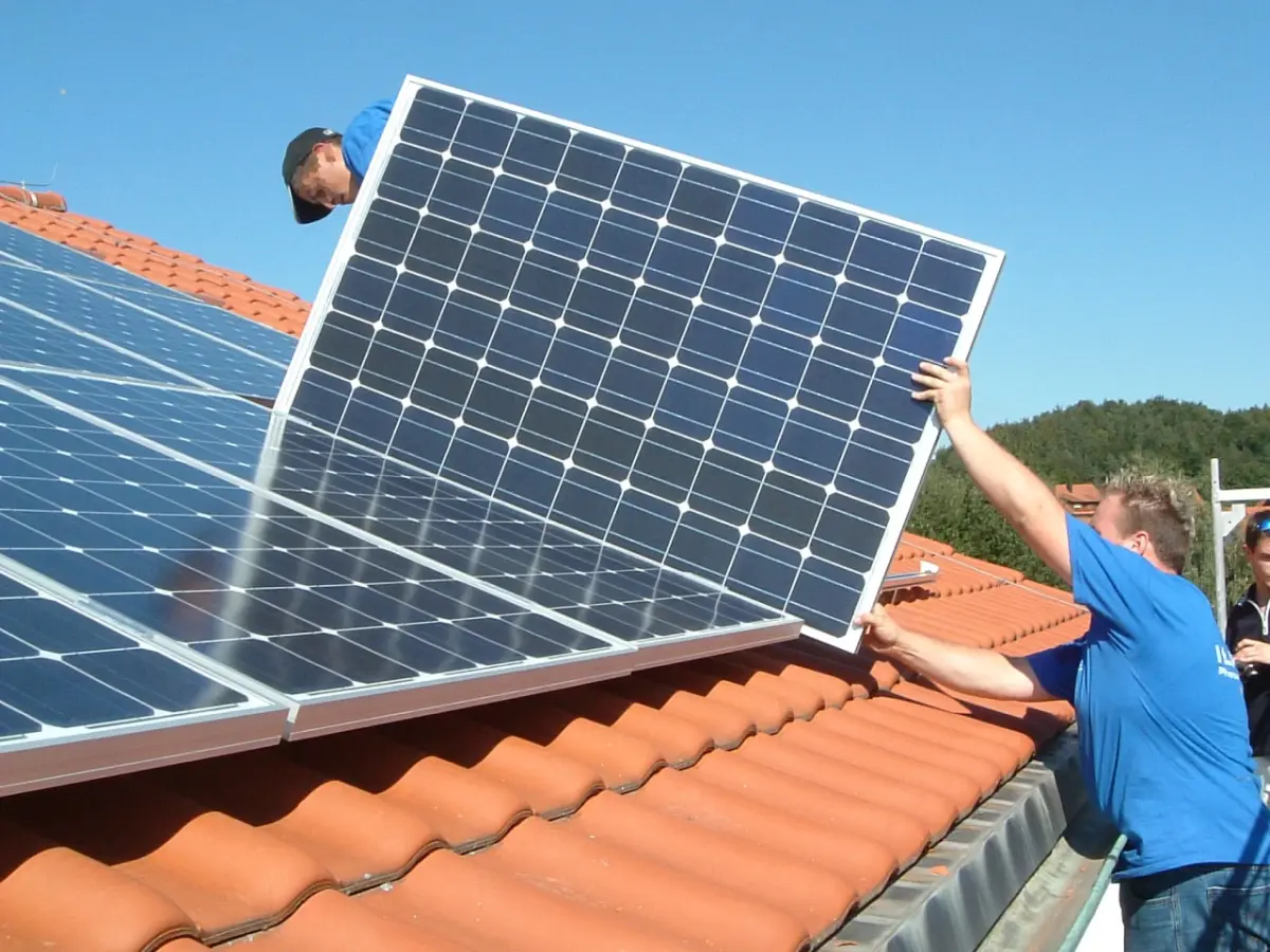 Zwei Männer montieren ein PV-Modul auf einem Dach bei gutem Wetter.