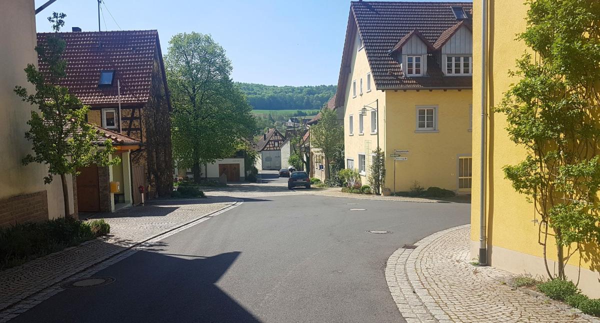 Dorfstraße. Links und rechts Häuser im ländlichen Stil mit Fassadenbegrünungen.