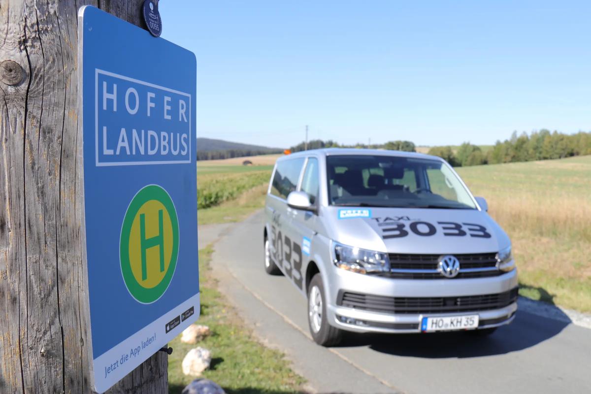 Hofer LandBus parkt auf einer Landstraße. Im Vordergrund ein blaues Haltestellenschild des Hofer LandBus