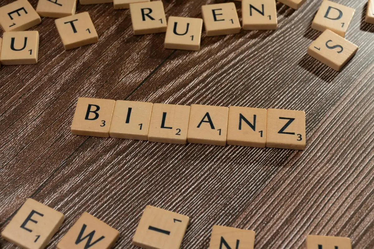 Holzsteinchen mit Buchstaben liegen auf Holtisch und bilden das Wort Bilanz.