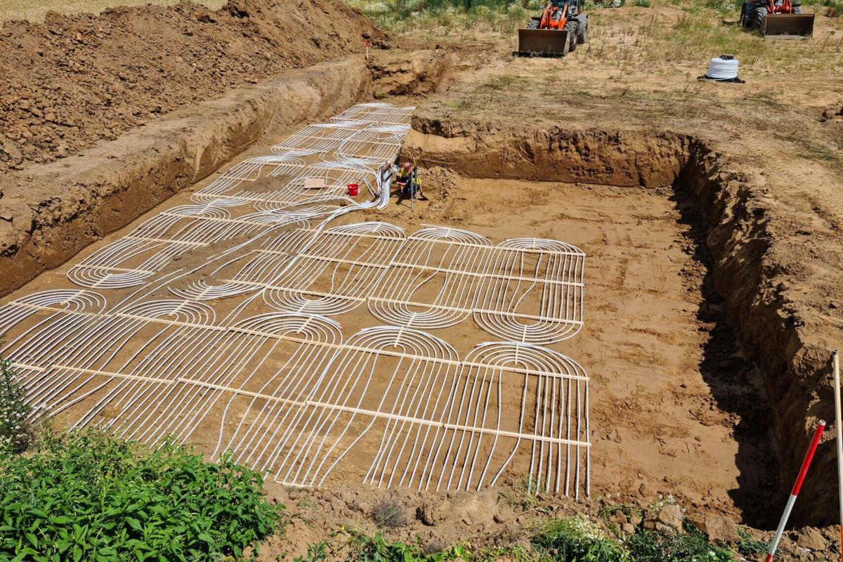 Mehrere Flächenkollektoren in einem Graben. Rechts hinten zwei rote Tracktoren.