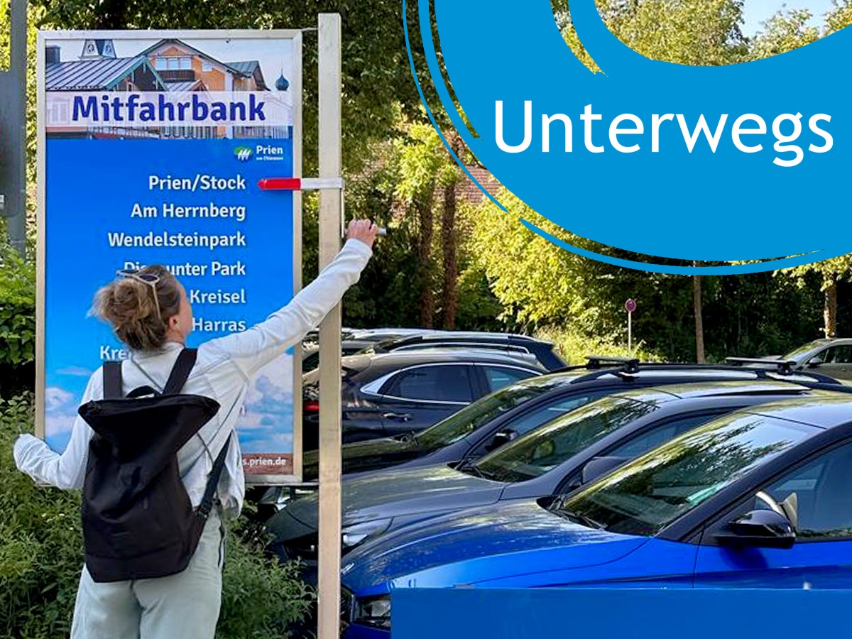 Frau steht vor Mitfahrschild, Schriftzug "Unterwegs"