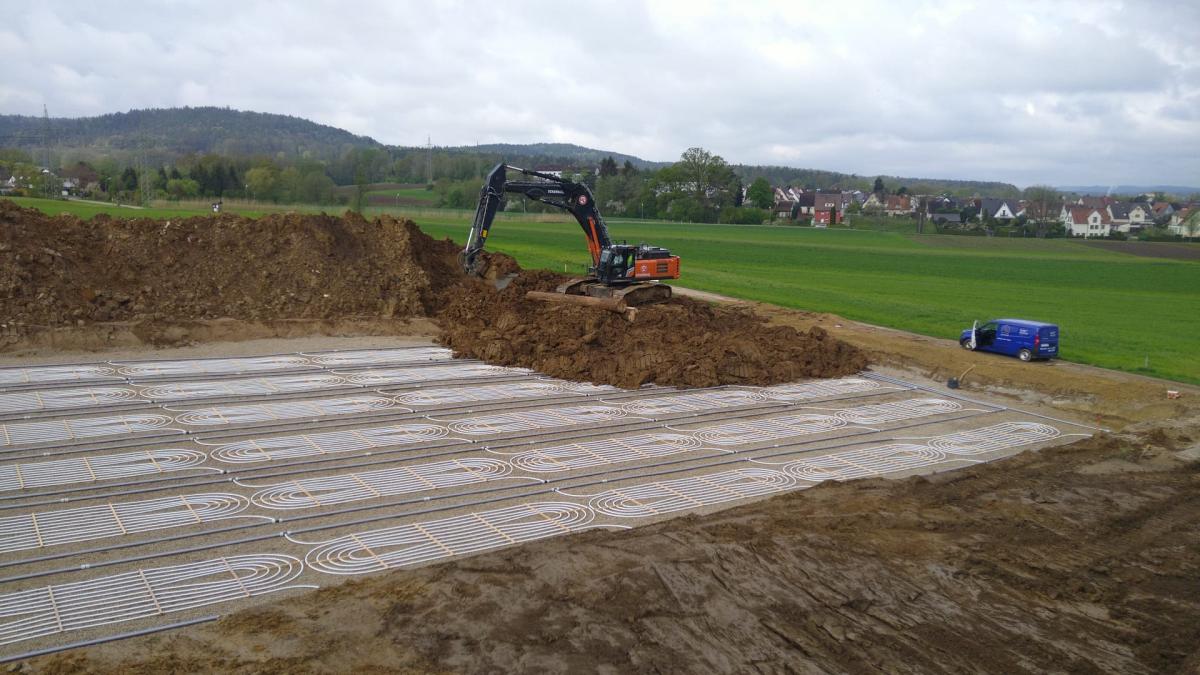 Horizontale Flachkollektoren in Erdaushub vor einem Dorf.