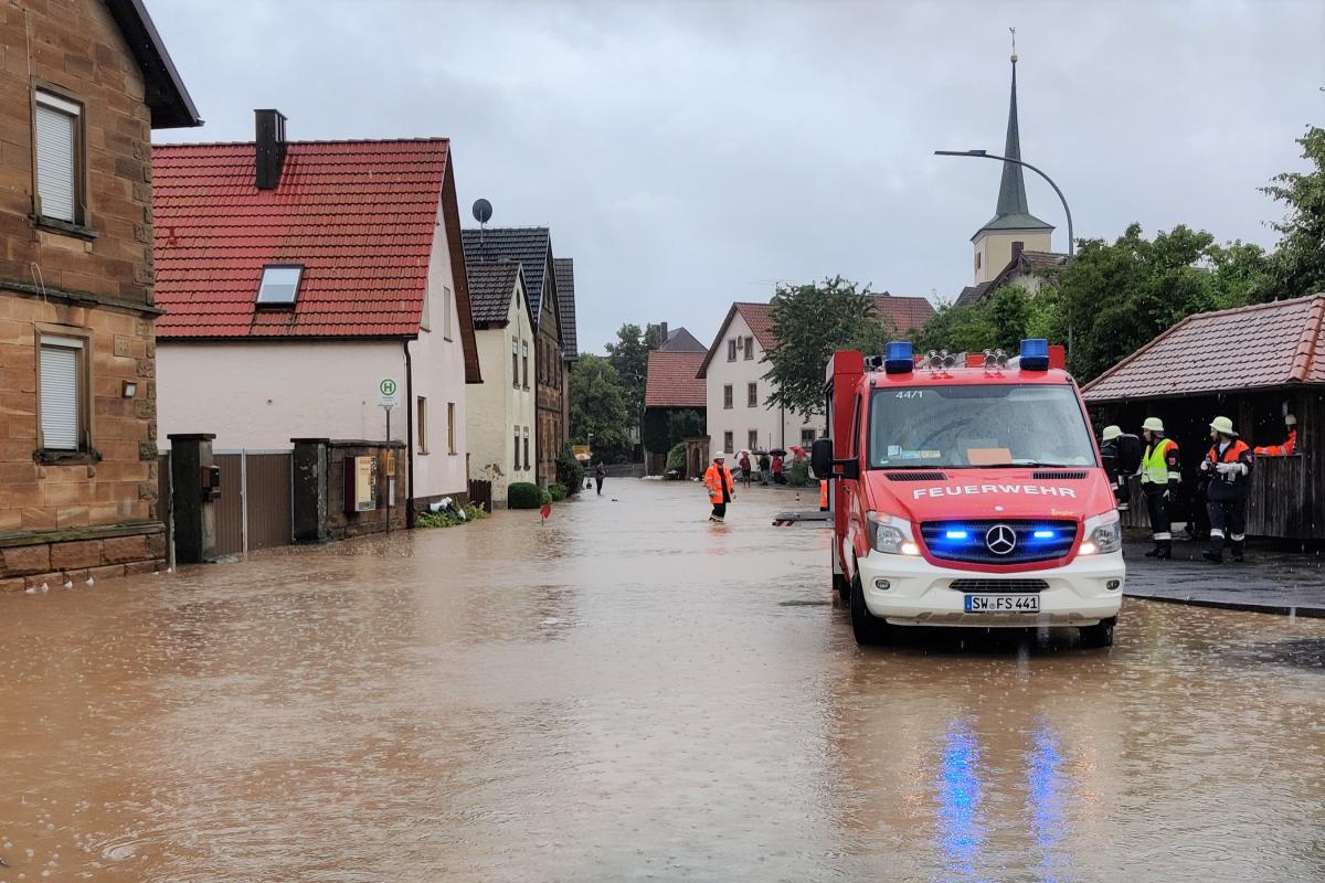 Überflutete DOrfmitte. Recht ein Feuerwehrauto.