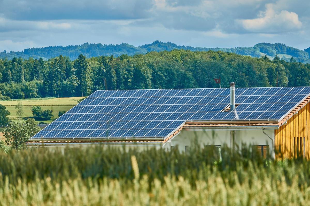 Solaranlage auf einem Hausdach im ländlcihen Raum. Im Hintergrund Wald. Im Vordergrund: Feld.