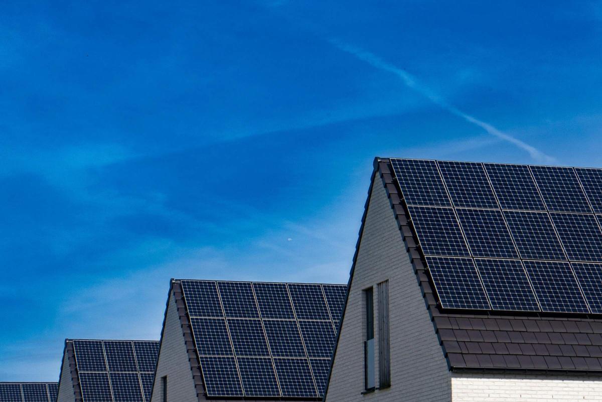 Vier Hausdächer mit Solarmodulen. Im Hintergrund blauer Himmel.