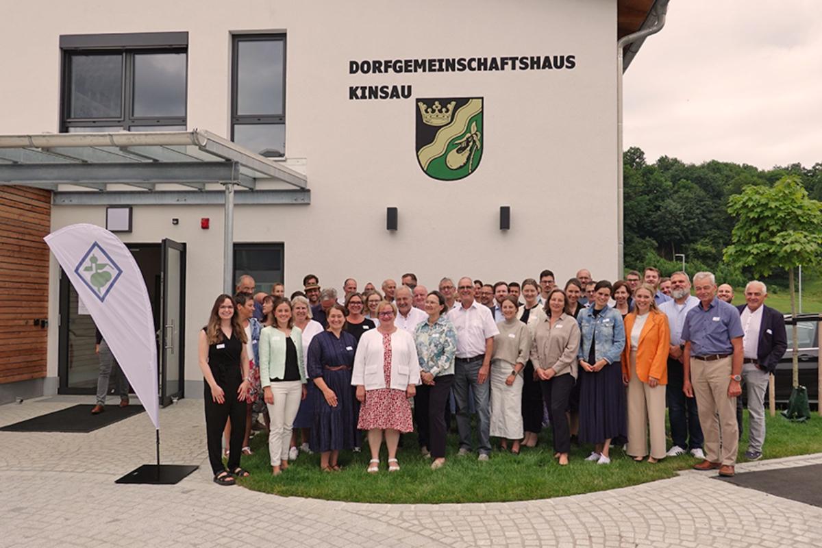 Personengruppe steht vor Haus und lächelt geschlossen in die Kamera