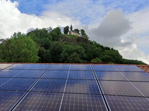 Photovoltaik-Module auf einem Dach, im Hintergrund ein grüner Hügel