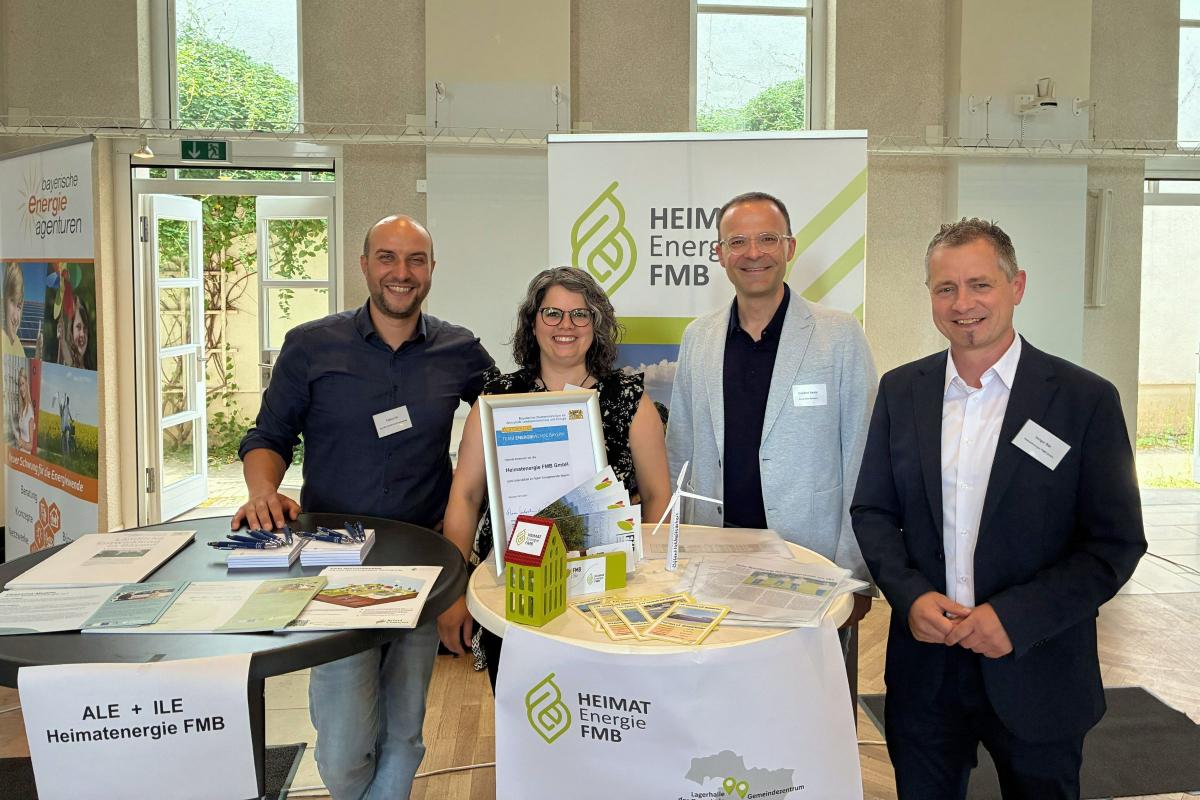 Eine Frau und drei Männer lächen in die Kamera vor einem Messestand.