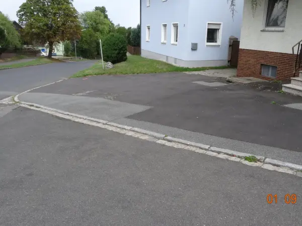 Asphaltierte Straßen und Gehwege. Im Hintergrund Häuser und Bäume.