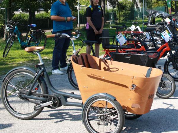 Mehrere Lastenfahrräder nebeneiander gereiht. Im Hintergrund Personen und Grünanlagen.