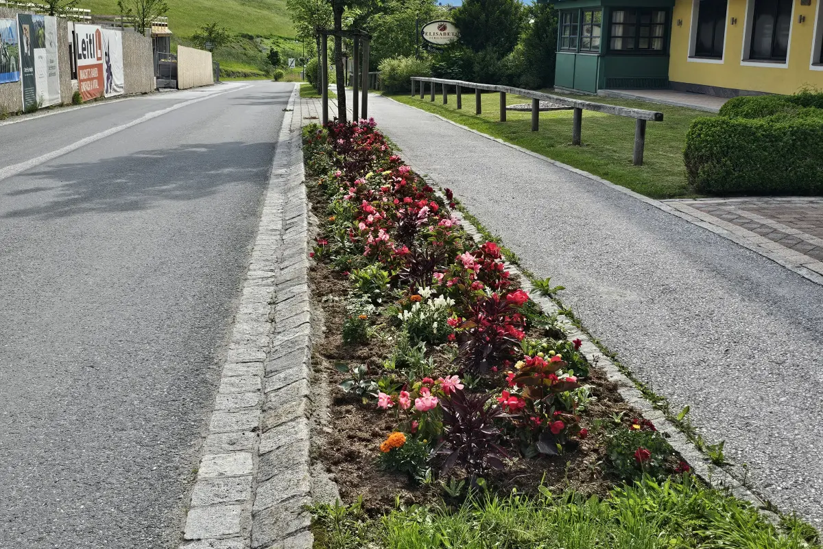 Links Straße, in der mitte ein bepflanzes Blumenbeet, rechts ein Gehweg.