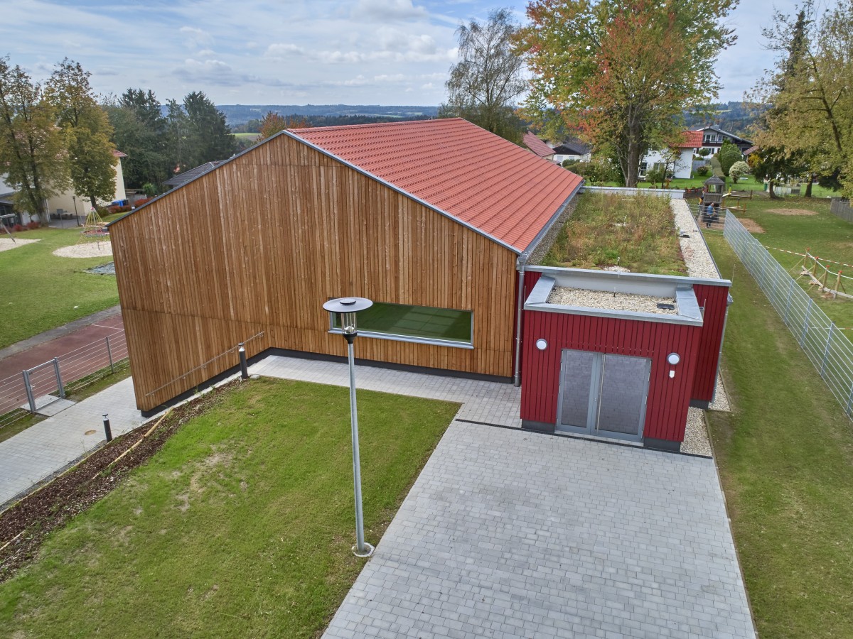 Holzhaus mit Carport. Darauf ein Gründach. Im Hintergrund Bäume. Im Vordergrund Rasenfläche.