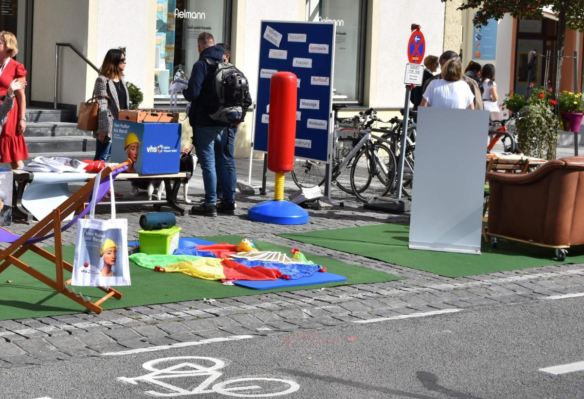 Im Vordergrund eine Fahrradstraße. Im Hintergrund ein umgenutzter Parkplatz mit Sitzgelegenheiten.