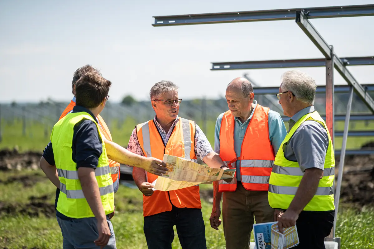 Fünf Männer stehen in Sicherheitswesten vor Gerüst eine Freiflächen-Photovoltaikanlage.