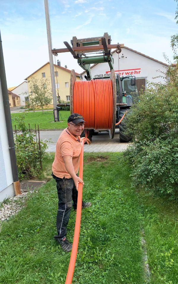 Man mit orangem T-Shirt steht auf einem Rasegrundsück und hält ein orangenes Rohr.