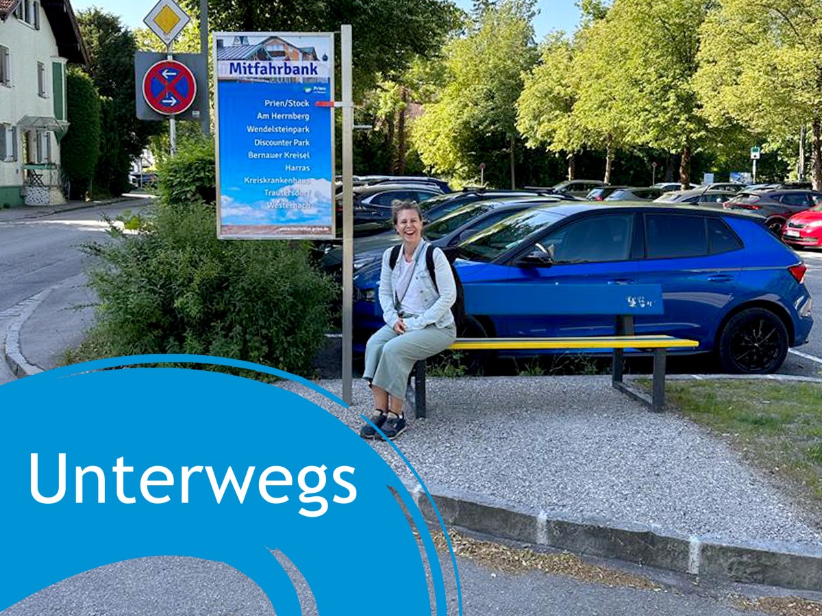 Frau sitzt auf Mitfahrbank, daneben der Schriftzug "Unterwegs"