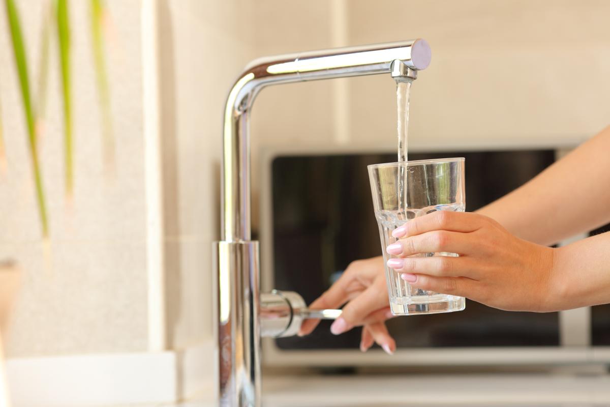 Frau füllt ein Glas mit Wasser aus dem Wasserhahn