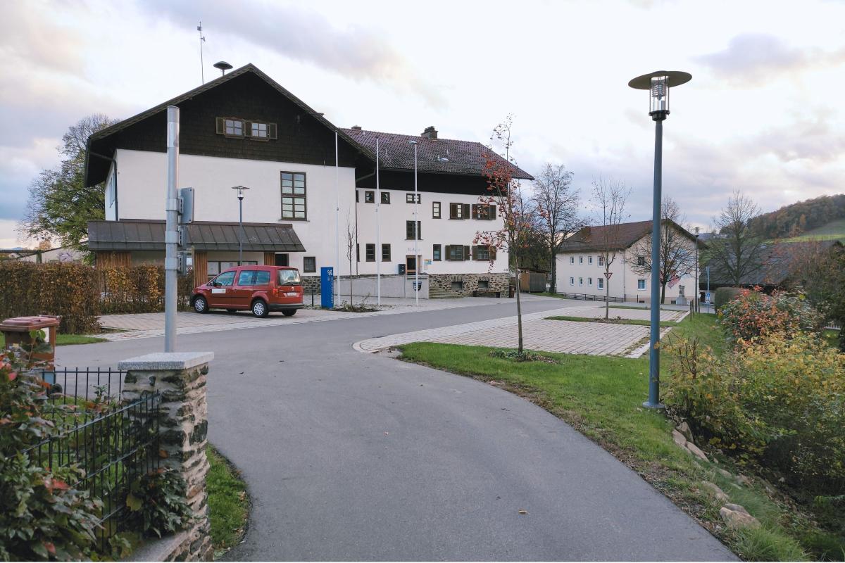 Haus im Hintergrund. Im Vordergrund Parkplatz und Straßenlaternen.