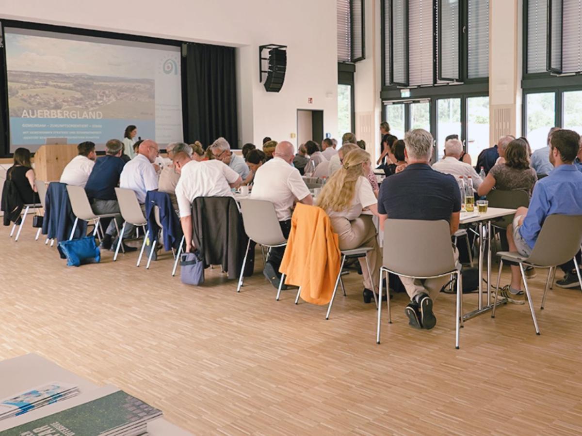 Personen sitzen an Tischen und sehen nach vorne zum Vortrag