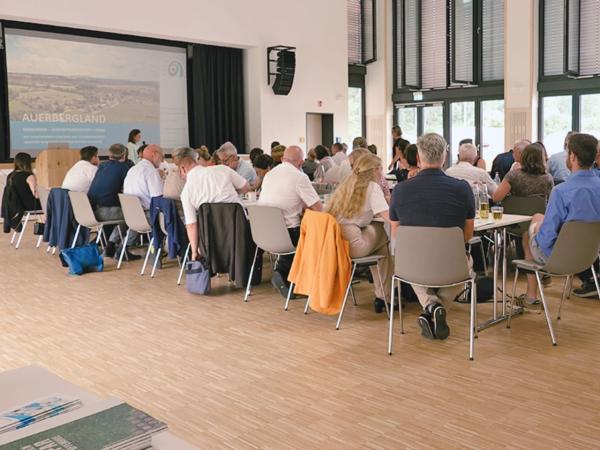 Personen sitzen an Tischen und sehen nach vorne zum Vortrag